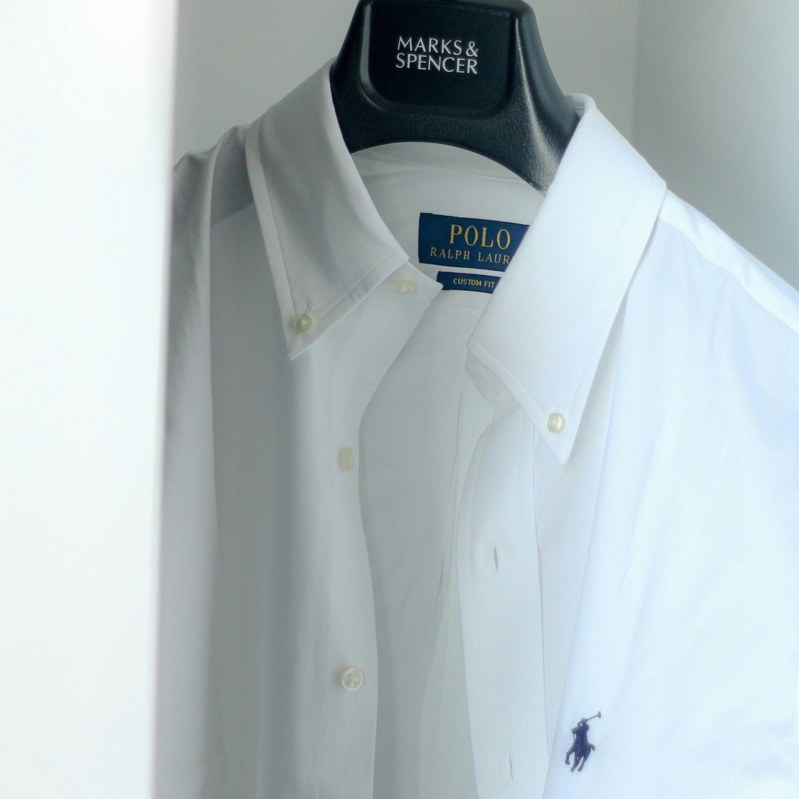 Crisp white Ralph Lauren polo shirt hanging in a modern minimalist wardrobe.