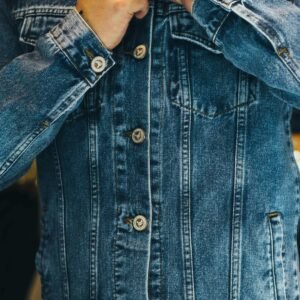 Close-up of a man fastening a denim jacket, showcasing fashion and style details.
