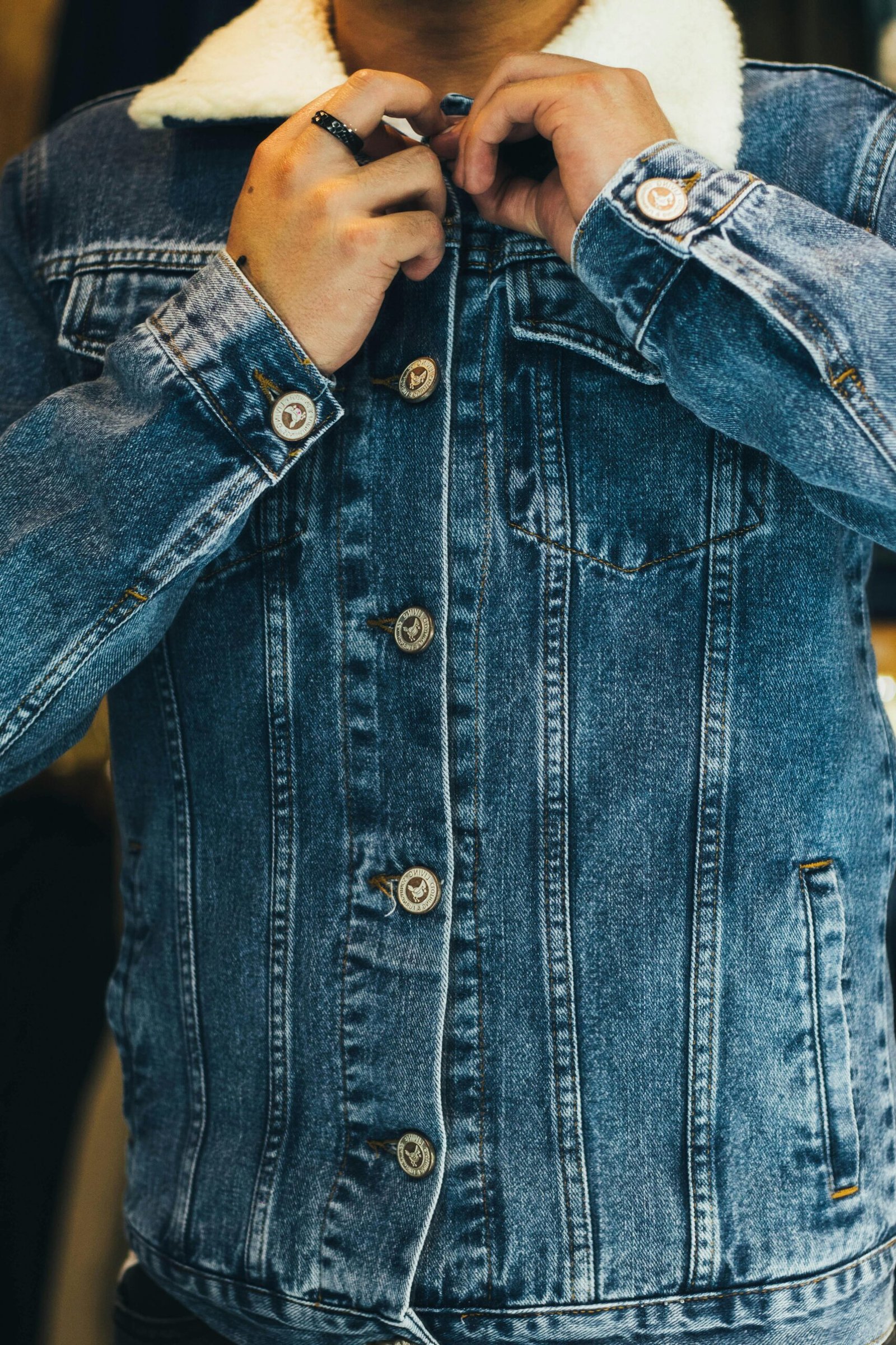 Close-up of a man fastening a denim jacket, showcasing fashion and style details.