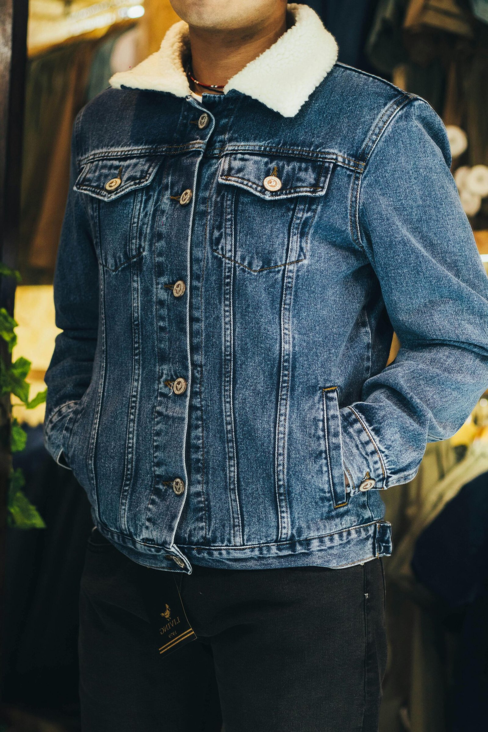 Man wearing a stylish denim jacket with white shearling collar, hands in pockets.